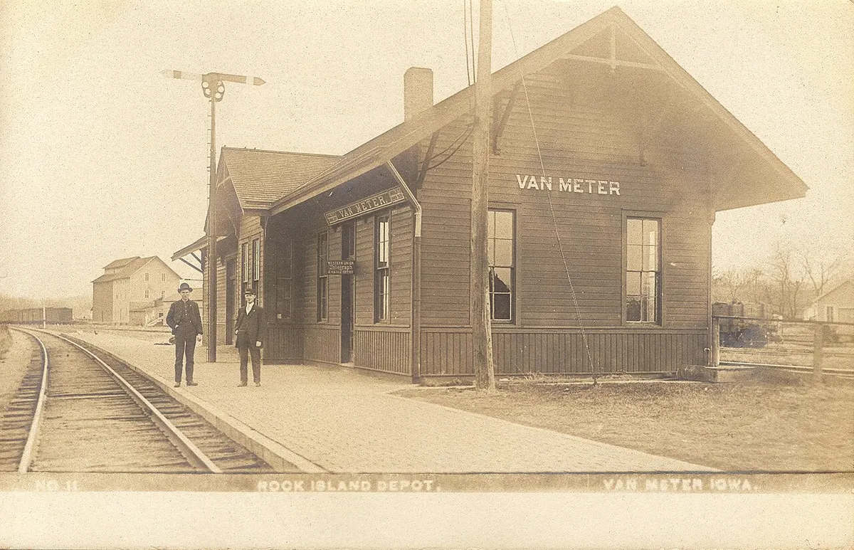 Early-1900s postcard of the Rock Island railroad depot in Van Meter, Iowa, with two railroad employees on the platform