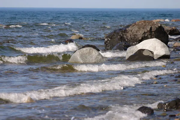 Waves breaking over rounded boulders along the shore of Iliamna Lake under a pale sky