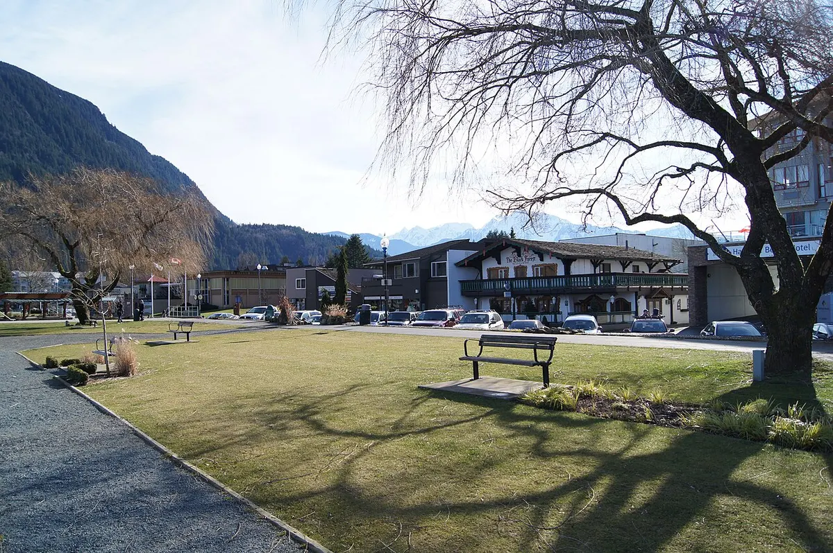 A lawn, path and bare trees along the waterfront park at Harrison Hot Springs, British Columbia, with hotels and steep mountains behind
