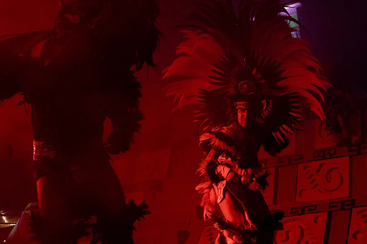 A dancer in a tall feathered headdress lit in deep red light on the La Llorona stage at Xochimilco