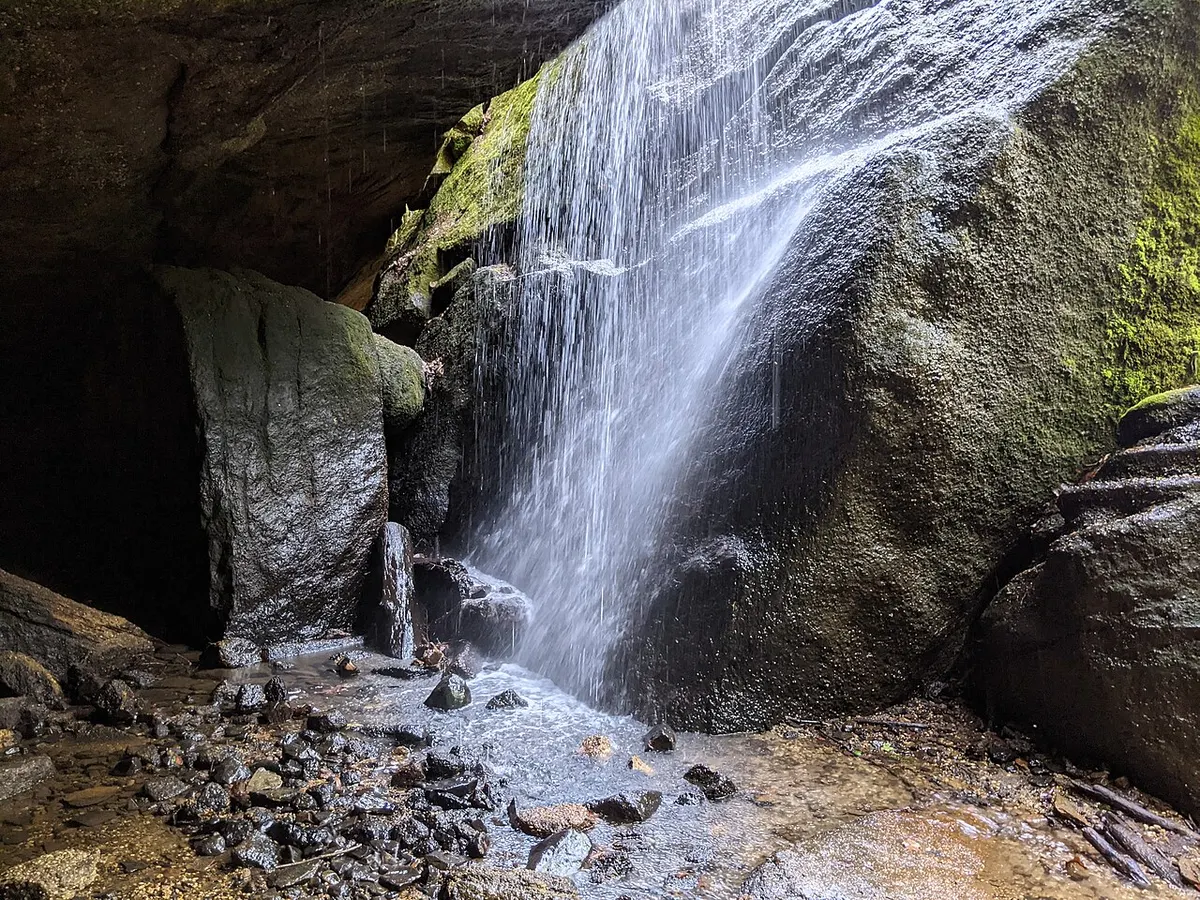 A small waterfall pouring over large, mossy sandstone boulders into a rocky pool at Nelson-Kennedy Ledges State Park