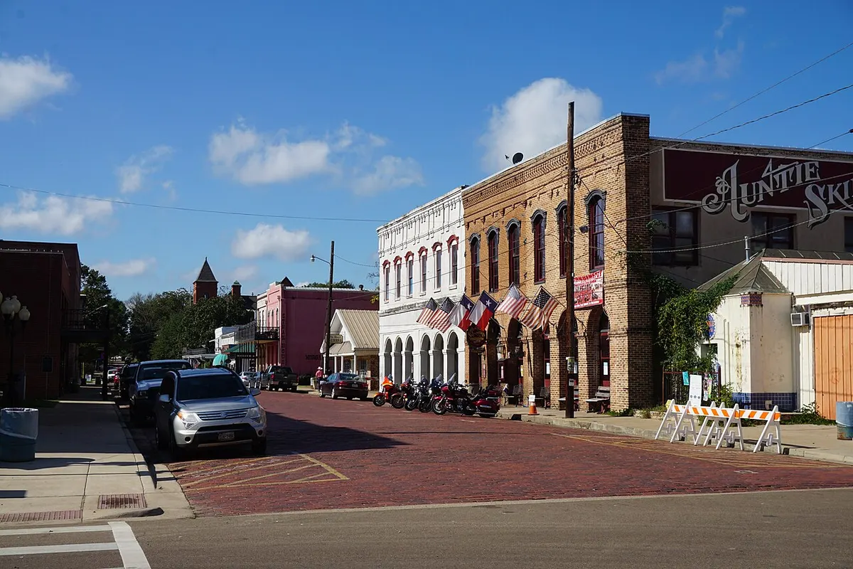 Historic brick and painted storefronts with American flags along a red-brick section of Austin Street in Jefferson, Texas